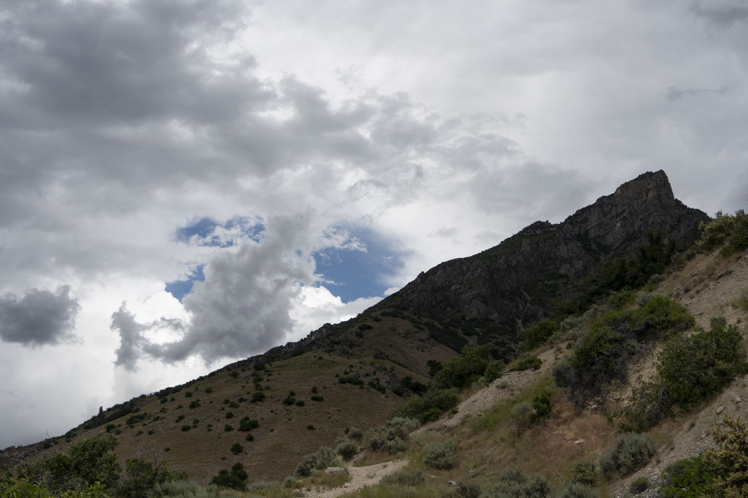 The mountains green and rocky against many overlapping white clouds with a blue gap